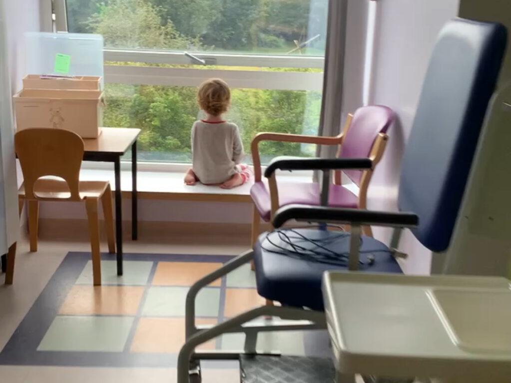 Felix as a small boy staring out of a big window in hospital with his back to us.